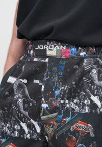 Μαύροι μπασκετικοί σορτς με διάτρητη υφή, διάσπαρτα γραφικά αποτυπώματα παικτών και ελαστική μέση με τη λέξη «JORDAN».
