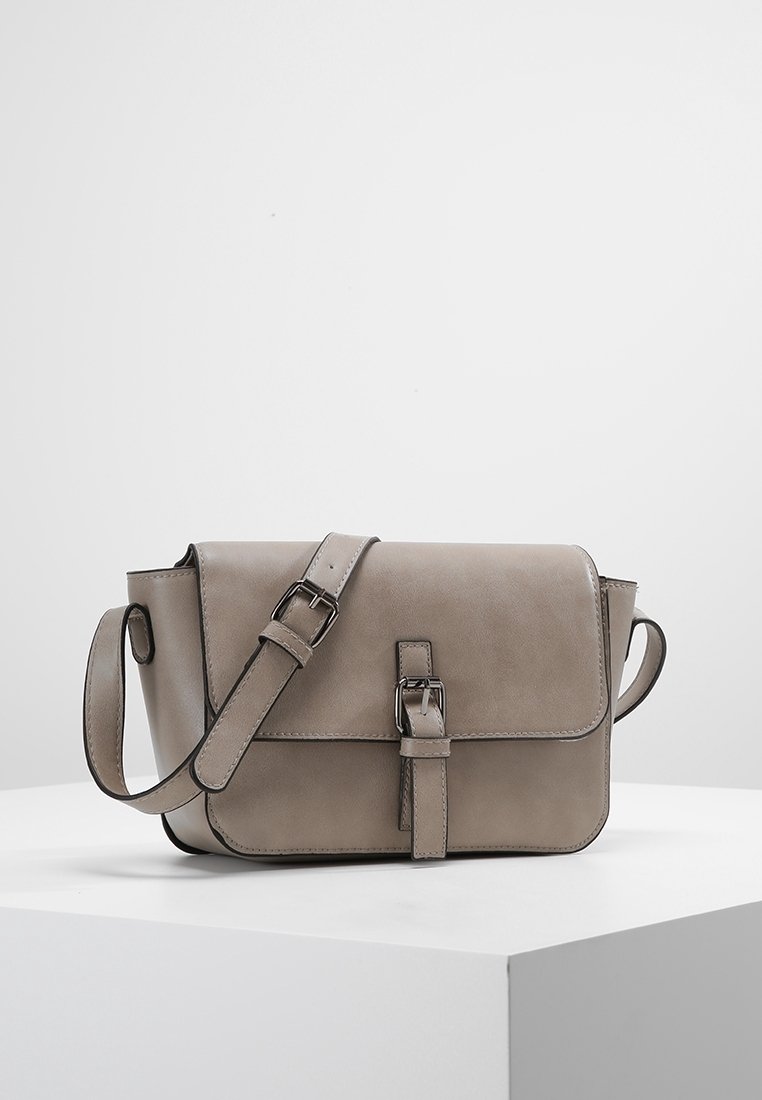 Taupe kožená křiž-crossbody taška s nastavitelným popruhem na přezku a detailní přezkou na přední straně, umístěná na bílé ploše a s neutrálním pozadím.