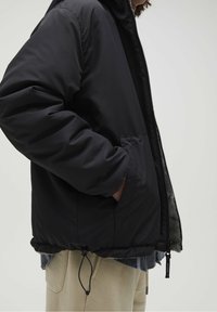 Czarna ocieplana kurtka z kapturem, elastycznymi mankietami i ściąganym dołem. Posiada boczne kieszenie i kontrastową podszewkę.