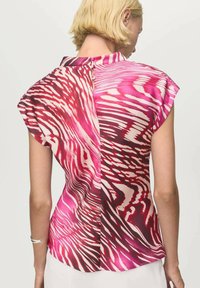 Blusa de manga corta con un vibrante patrón abstracto en rosa y rojo, tejido fluido y un sutil detalle de costura en la parte posterior.