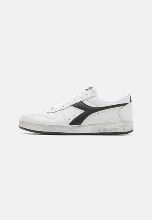 Baskets en cuir blanc avec des accents noirs, détails perforés, lacets plats et logo sur le côté. Semelle en caoutchouc légèrement texturée.