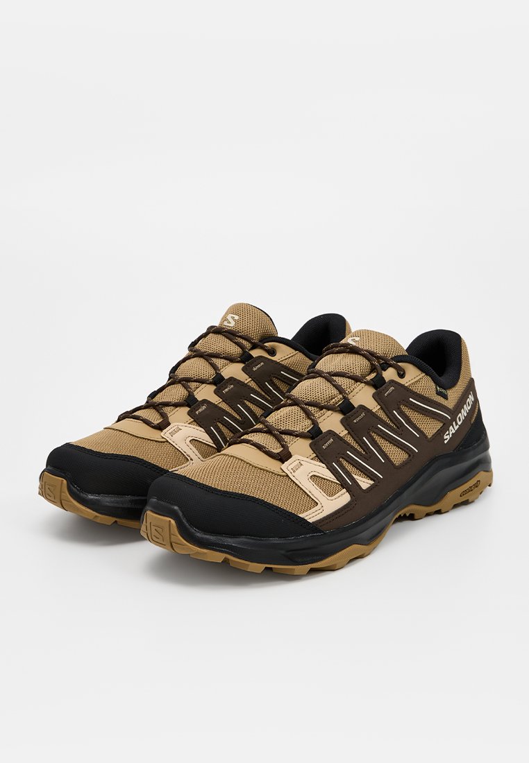 Zapatillas deportivas en tonos marrón y negro con parte superior de malla y sintético, que cuentan con una suela texturizada, sistema de cordones y acentos en contraste.