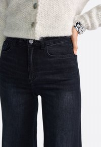 Črne visokogrežne kavbojke s slim fit krojem, opremljene z gumbom, sprednjimi žepi in gladkim denim materialom.