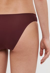 Costum de baie inferioare burgund dintr-o textură mată, netedă. Designul cu talie joasă oferă o acoperire minimă și un finisaj curat la talie.