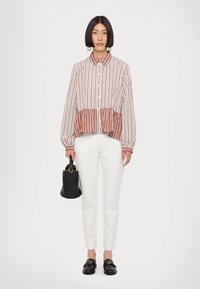 Striped blouse with a button front, featuring a ruffled hem. Paired with tailored white trousers and black loafers. Accessory: black handbag.