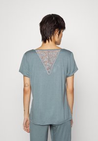 Haut à manches courtes, coupe décontractée en bleu sarcelle atténué avec un panneau en dentelle triangulaire au dos. Tissu lisse sans motifs, design simple.