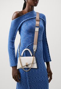 Weiße Mini-Handtasche mit Krokodilprägung, Top-Griff und Kettenriemen, kombiniert mit einem blauen, gerippten Kleid mit asymmetrischem Ausschnitt.