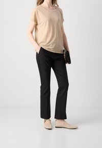 Top beige de manga corta con cuello redondo, pantalones negros a medida y zapatos planos de un beige claro con una correa alrededor del tobillo.