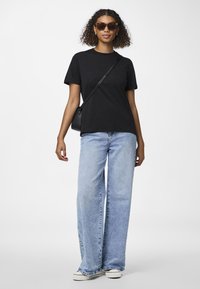 Fekete pamut póló, lazább szabású. Világoskék, bő szárú farmernadrág, elhalványult textúrával. Kiegészítők közé tartozik a sötét mintás napszemüveg és egy kis fekete táska.