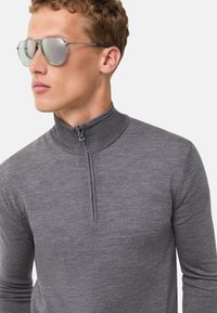 Grau zip-necks Pullover aus einem weichen Strickstoff. Verfügt über einen hohen Kragen und lange Ärmel. Reflektierende Sonnenbrille mit Metallrahmen.