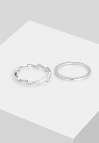 Zwei silberne Ringe: Der eine hat ein Zickzack-Muster mit kantigen Ausschnitten, der andere ist ein glatter, schlichter Ring. Beide sind poliert und glänzend.