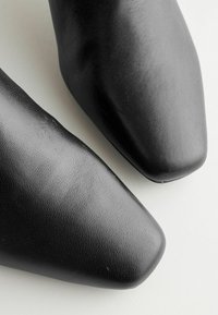 Schwarze Lederschuhe mit glatter Textur, quadratischer Zehenform und minimalistischem Design; aus einem Winkel betrachtet, der die obere Fläche hervorhebt.