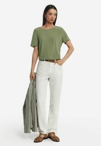 Olivgrön topp med kort ärm, krämfärgade vida byxor, brun bälte, grått texturerat cardigan hängande över armen och bruna sandaler.