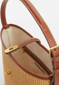 Kudottu olkasalkku ruskeilla nahkaosuuksilla, sileä vaaleanbeige sisus ja kultaiset metalliosat. Varustettu säädettävällä olkahihnalla.