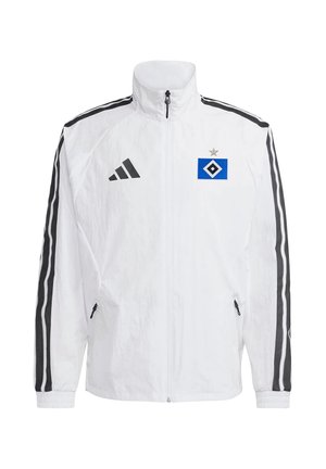 Biała kurtka sportowa z czarnymi paskami na rękawach, czarnym zamkiem błyskawicznym, logo Adidas na prawej piersi oraz niebieskim logo drużyny sportowej z gwiazdą na lewej piersi.