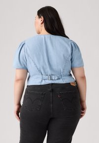 Top in denim blu chiaro con maniche a sbuffo corte, vita cinta da una cintura e cucitura a V sulla parte posteriore, abbinato a jeans neri a vita alta con tasche curve.