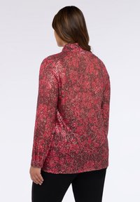 Top lungo con maniche a sbuffo in tonalità di rosa con motivo floreale; presenta un colletto alto e una vestibilità rilassata, abbinato a pantaloni neri.