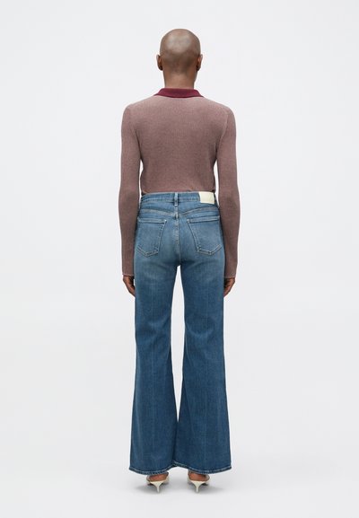 Καρυδί ριχτό μπλουζάκι με μακρύ μανίκι και μπορντό γιακά, συνδυασμένο με φαρδιά τζιν παντελόνια σε μπλε απόχρωση. Ξεχωριστή λεπτομέρεια στην πίσω τσέπη των παντελονιών.