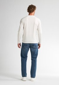 Camisa de manga larga crema, jeans de mezclilla azules, zapatos casuales de color claro. Diseño estructurado con un corte estándar y estilo minimalista.