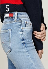 Vaqueros de denim azul claro de cintura alta, con una etiqueta de Tommy Jeans, bolsillos traseros y un ligero desgastado.