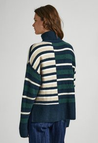 Maglione a collo alto a righe con strisce di diverse larghezze in blu navy, verde e crema. Tessuto a maglia morbida, vestibilità ampia e orlo a coste.