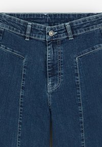 Mørkeblå denimjeans med klassisk pasform, der har kontrasterende syninger og en metalknaplukning ved taljen.