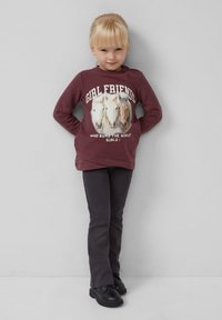 Burgundowa bluza z długim rękawem z grafiką koni i napisem "GIRL FRIENDS". W połączeniu z ciemnoszarymi spodniami i czarnymi butami.