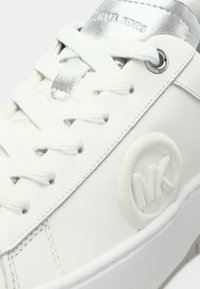 Λευκό αθλητικό παπούτσι με λείο δέρμα στην επάνω επιφάνεια, ασημί λεπτομέρεια στη γλώσσα, λευκά κορδόνια και ανάγλυφο λογότυπο MK στο πλάι. Υφή με λεπτομέρειες στη σόλα.