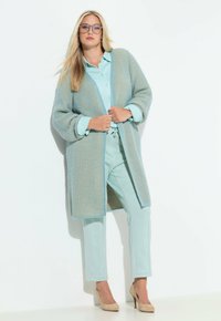 Hellblauer Strickcardigan mit Rippenstruktur, offene Vorderseite, kombiniert mit einem hellblauen Hemd und passenden Hosen, vervollständigt mit beigen Absätzen.