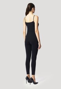 Svart åtsittande linne och leggings med justerbara axelband, kombinerat med svarta högklackade skor. Slät textur, figurnära design.