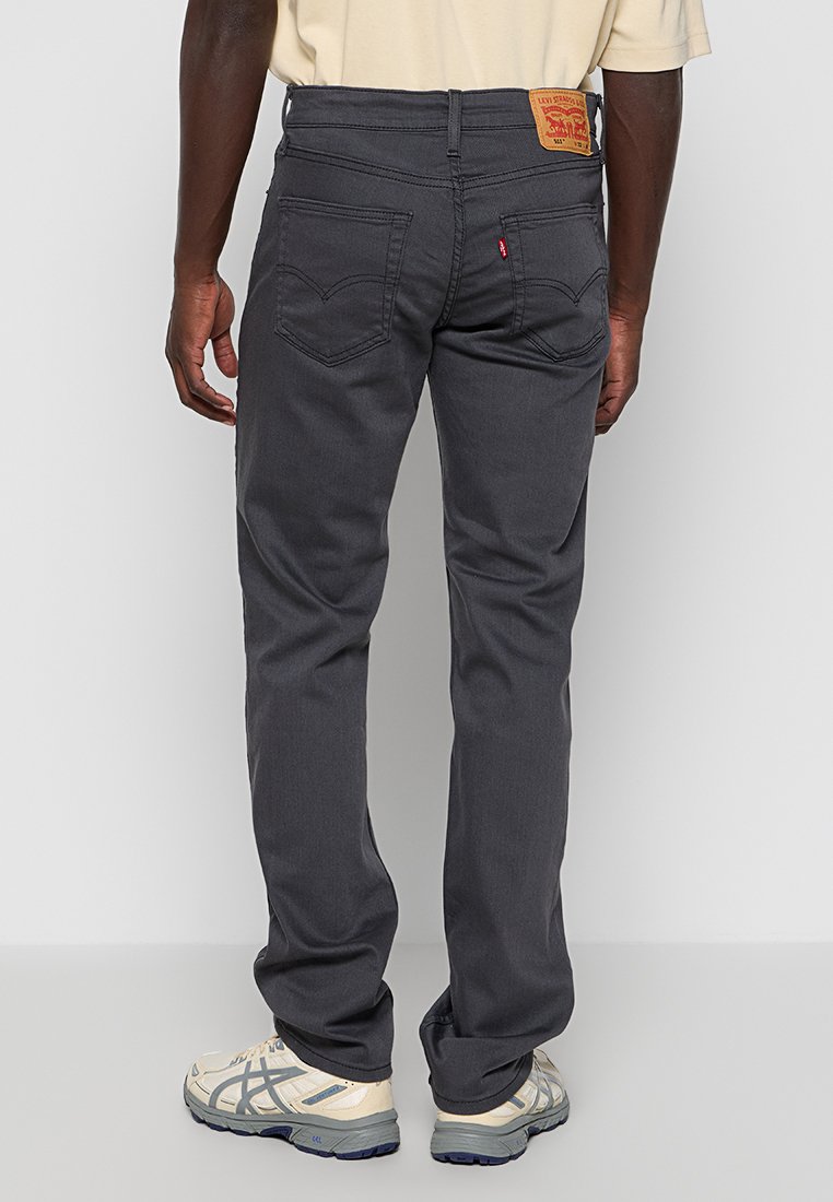 Grijze denim jeans met een rechte pasvorm, met achterzakken en een geborduurd logo op de tailleband. Draagt met lichtgekleurde sneakers.