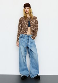 Krótki sweter w panterkę, niebieskie szerokie spodnie z wysokim stanem i sznurkiem oraz czarne obuwie. Delikatne tekstury materiałów i luźny krój.