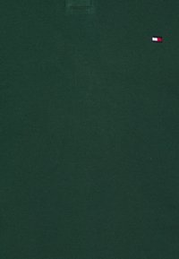 Tmavě zelená polokošile z texturované bavlny. Na levé straně hrudi má malou červenou, bílou a modrou značku. Klasický design s límečkem.