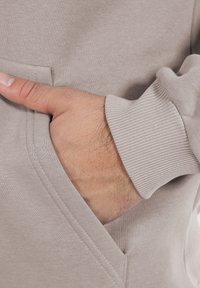 Grijze hoodie met een voorzak en ribgebreide manchetten. De stof heeft een zachte textuur, met nauwkeurige stiksels en zichtbare schone lijnen.