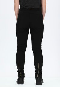 Zwarte broek met een slim fit, voorzien van een zachte textuur, ritsen bij de enkels en een gouden accent op de tailleband. Ontworpen voor comfort en bewegingsvrijheid.