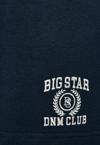 Jūras zilas kokvilnas audums ar teksturētu adījumu. Iezīmēts ar baltu izšuvumu, kas lasāms "BIG STAR DNM CLUB", un dekoratīvām lauru akcentiem.