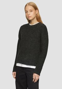Donkergrijze gebreide trui met een ronde hals, geribbelde manchetten en een relaxte pasvorm, gedragen over een wit shirt, gecombineerd met zwarte broek.