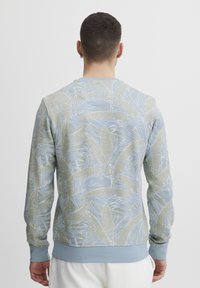 Lyseblå sweatshirt med et grønt og hvidt bladmønster, rund hals, lange ærmer og ribbede manchetter. Blødt stof.