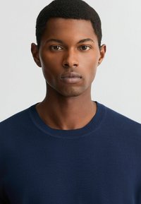 Marineblå sweater med ribbet crew neckline, der har en glat tekstur og en tætsiddende pasform. Ingen synlige logoer eller mønstre.