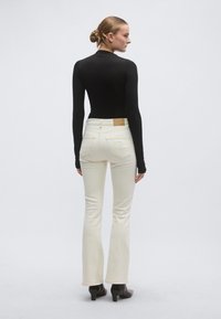 Μαύρη μπλούζα με μακριά μανίκια συνδυασμένη με κρεμ παντελόνι τζιν καμπάνα. Το τζιν διαθέτει δερμάτινη ετικέτα στην πίσω πλευρά και διακριτικές λεπτομέρειες ραφής.