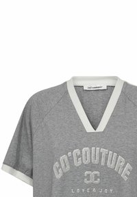 Pilkas medvilninis marškinėliai su V formos iškirpte, balta apdaila ir trumpomis rankovėmis. Papuoštas sidabro spalvos spausdintu "GO'COUTURE LOVE & JOY" logotipu.