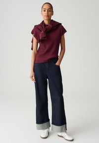 Burgundy ribbed short-sleeve top with a knitted texture, paired with wide-leg dark denim jeans featuring a light blue cuff and white sneakers.