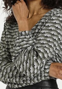 Grün gemusterte Bluse mit weißen Fächerdesigns, V-Ausschnitt, langen Puffärmeln und Knopfverschluss an den Manschetten. Strukturierten Stoff.