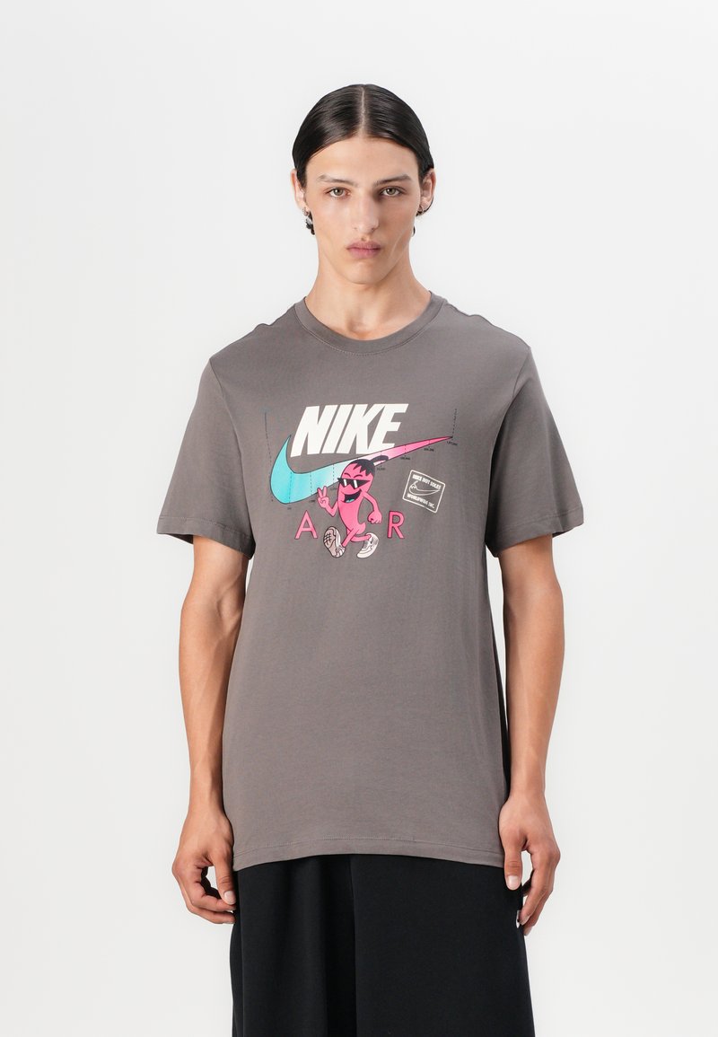 Šedé bavlněné tričko s krátkým rukávem. Na přední straně má velké barevné logo Nike a kreslenou grafiku. Design s kulatým výstřihem.