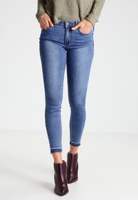 Modré denimové skinny džíny s vysokým pasem, s knoflíkovým zapínáním, dvěma předními kapsami a roztrhaným lemem na kotnících.