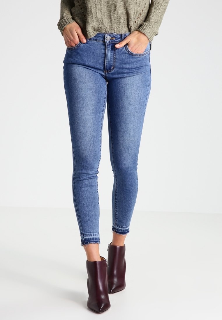 Modré denimové skinny džíny s vysokým pasem, s knoflíkovým zapínáním, dvěma předními kapsami a roztrhaným lemem na kotnících.