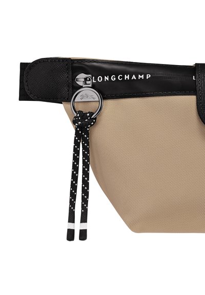 Beige nylon pouch with black accents, featuring a zipper closure, Longchamp logo, and a decorative cord with polka dots.