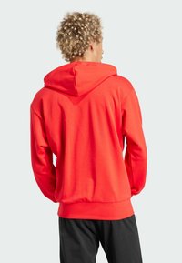 Felpa rossa con cappuccio regolabile, maniche lunghe e polsini a coste, realizzata in materiale morbido, con una vestibilità comoda. Pantaloni neri.