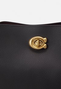 Surface en cuir noir texturé avec un gros plan d'un fermoir tournant ovale doré sur un sac à main ou un accessoire.