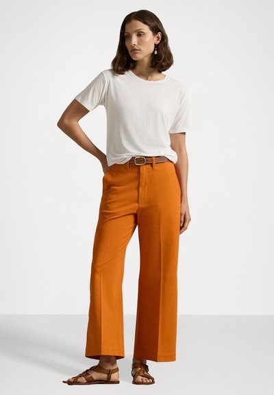 White t-shirt paired with high-waisted, wide-leg orange trousers. Trousers feature a belted waist and a smooth fabric texture. Flat sandals.